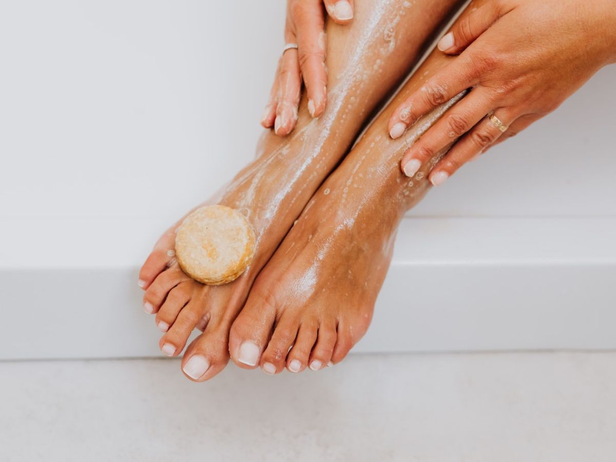 A pair of lady feets on the edge of a bathtub freshly lathered with a bar of soap